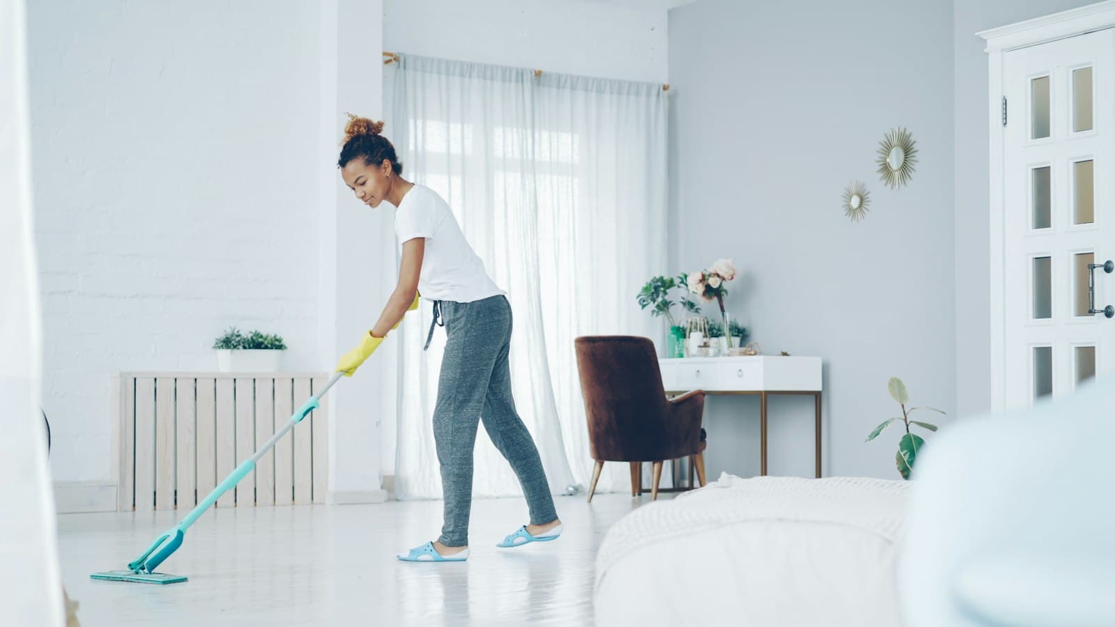 A cleaner in yellow rubber gloves mopping the floor of a bright living room